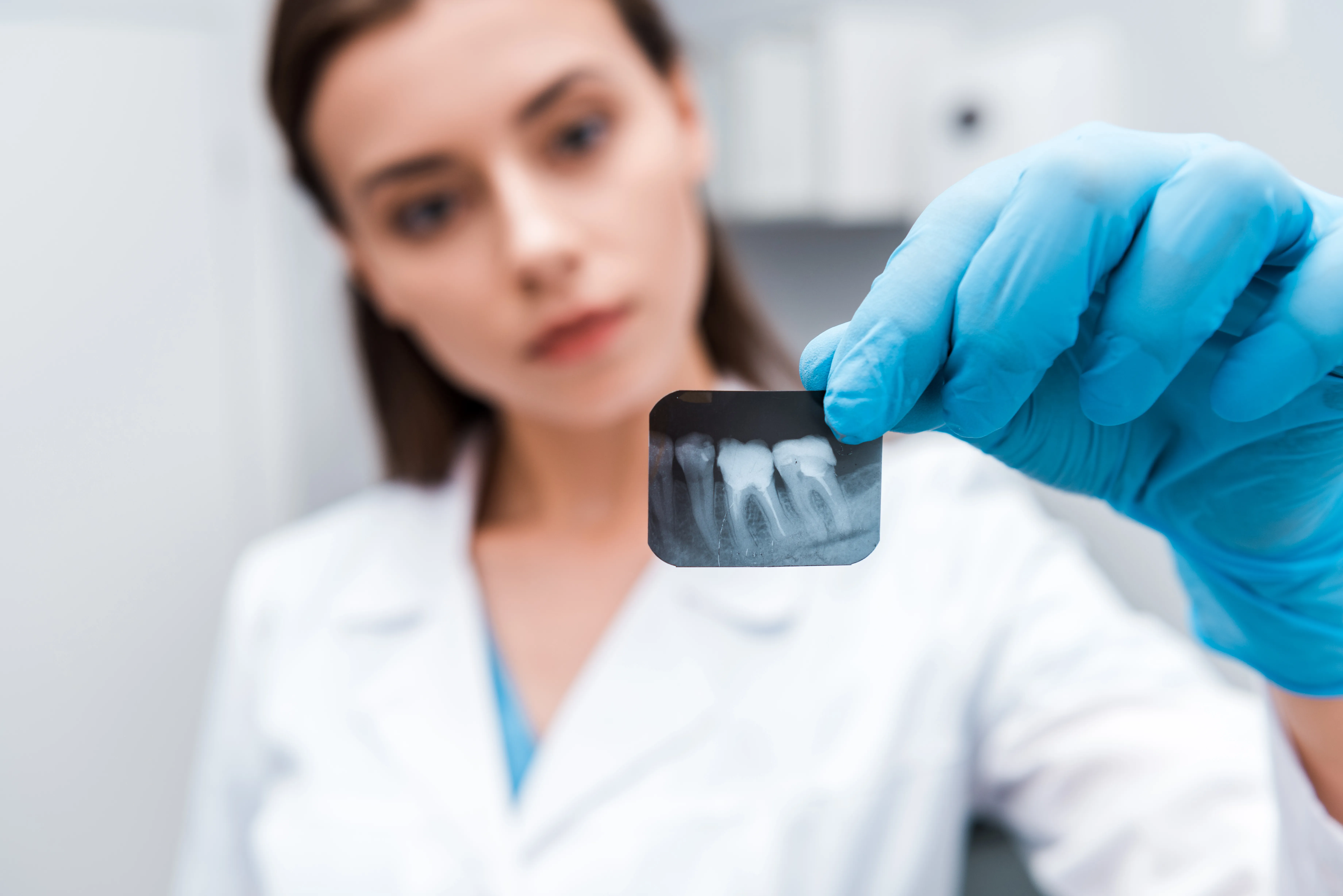 Dentista profesional sosteniendo radiografía periapical en clínica dental, cumpliendo estrictamente las normas de protección radiológica rayos X requeridas.
